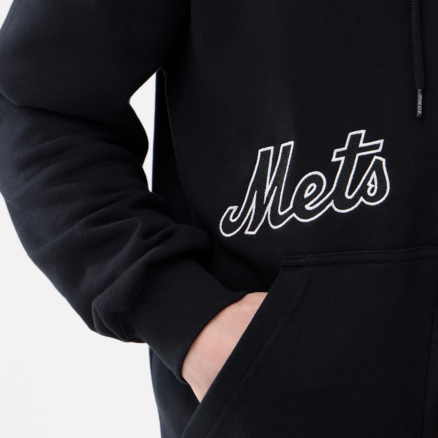 New Era New York Mets MLB Comfort Black 2 Way Full Zip Hoodie, on-model view showing the white embroidered 'Mets' logo on the lower front, long sleeves with ribbed cuffs, and a hand tucked into the pocket.