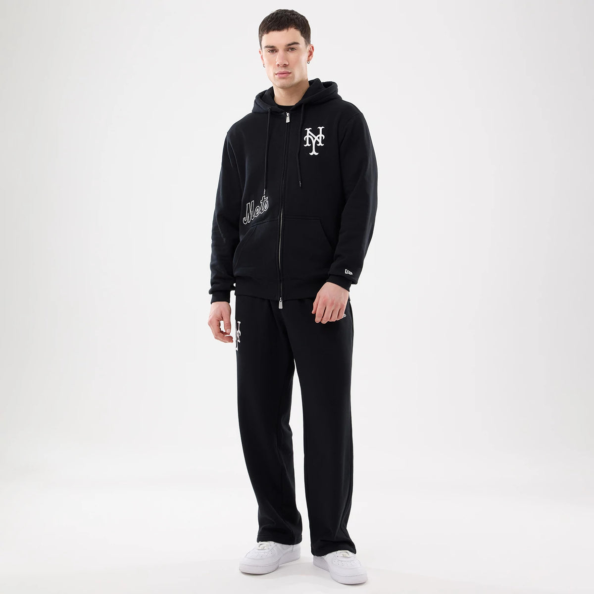 New York Mets MLB Comfort Black 2 Way Full Zip Hoodie, on-model view showing a black hoodie with a white Mets logo embroidered on the left chest, a full zip down the middle, and ribbed cuffs.
