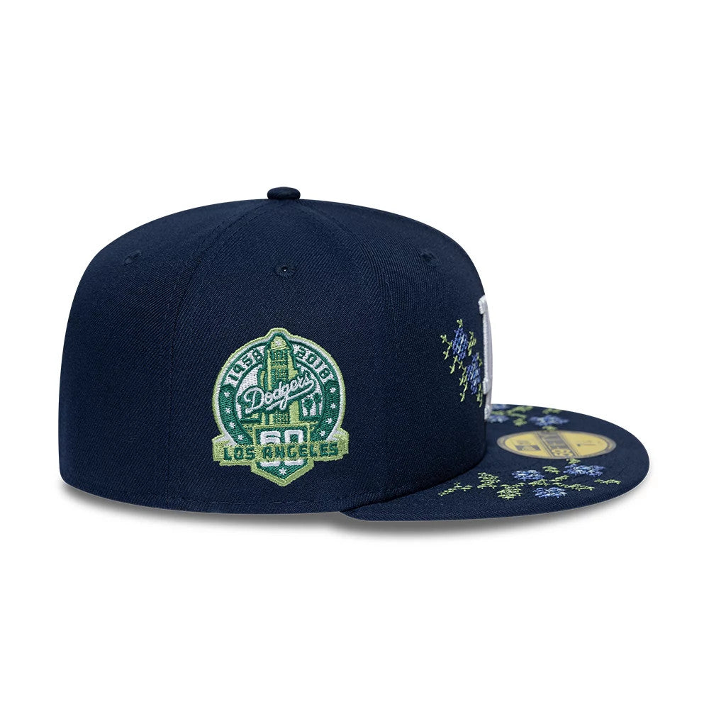 LA Dodgers MLB Garden Dark Blue New Era 59FIFTY Fitted Cap, side view showing a green 60th anniversary patch on the right panel, with floral embroidery across the visor and crown, and a gold 59FIFTY size sticker on the visor.