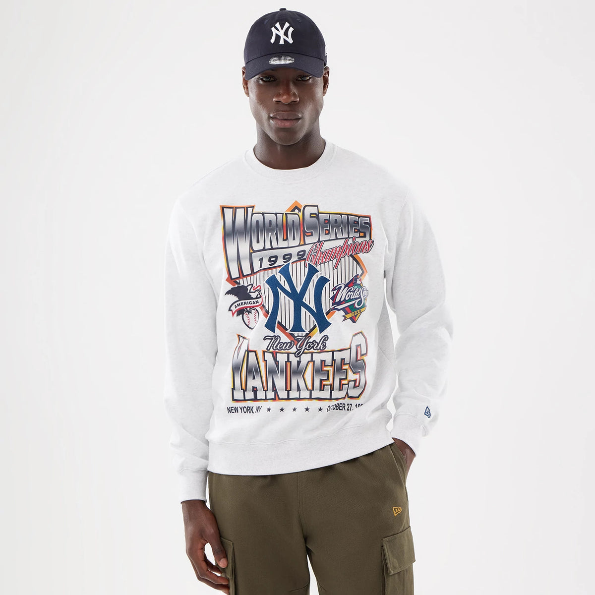 New York Yankees MLB Retro White Oversized Crew Neck Sweater, front view on a model with a navy Yankees cap, featuring bold World Series 1999 graphics and branding across the chest.