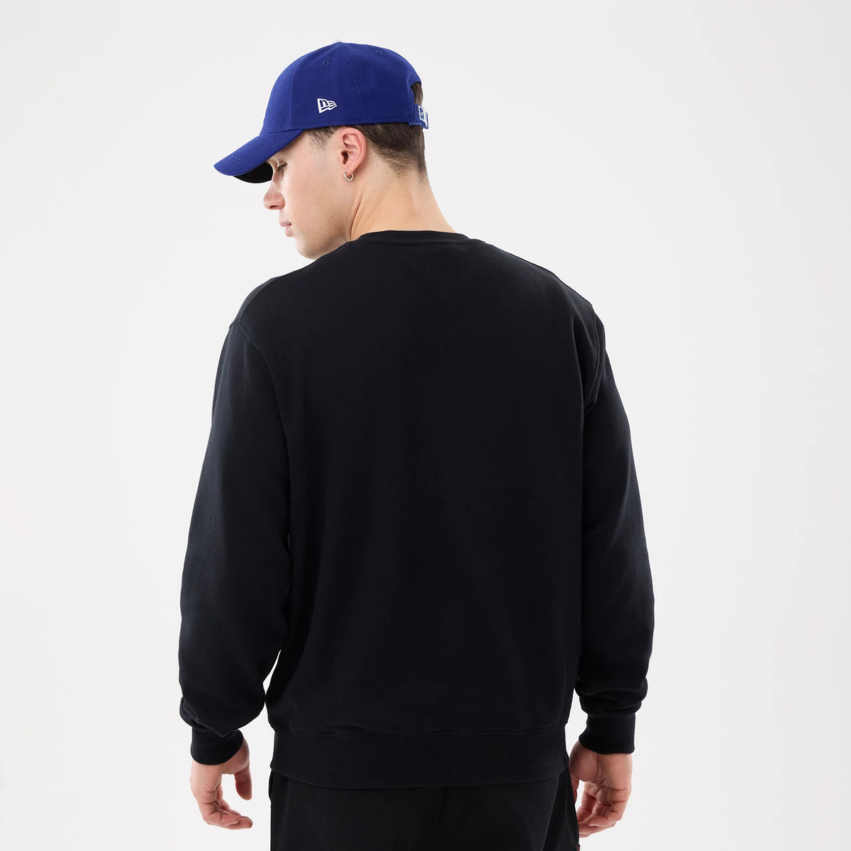 LA Dodgers MLB Retro Black Oversized Crew Neck Sweater, back view on a model wearing a blue cap with a New Era flag logo on the left side, highlighting the relaxed fit and ribbed cuffs of the sweater.