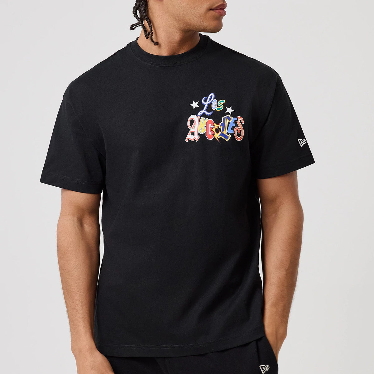 LA Dodgers MLB Word Art Black T-Shirt, on-model view showing the black fabric with colourful "Los Angeles" word art across the chest and a white embroidered New Era logo on the left sleeve.