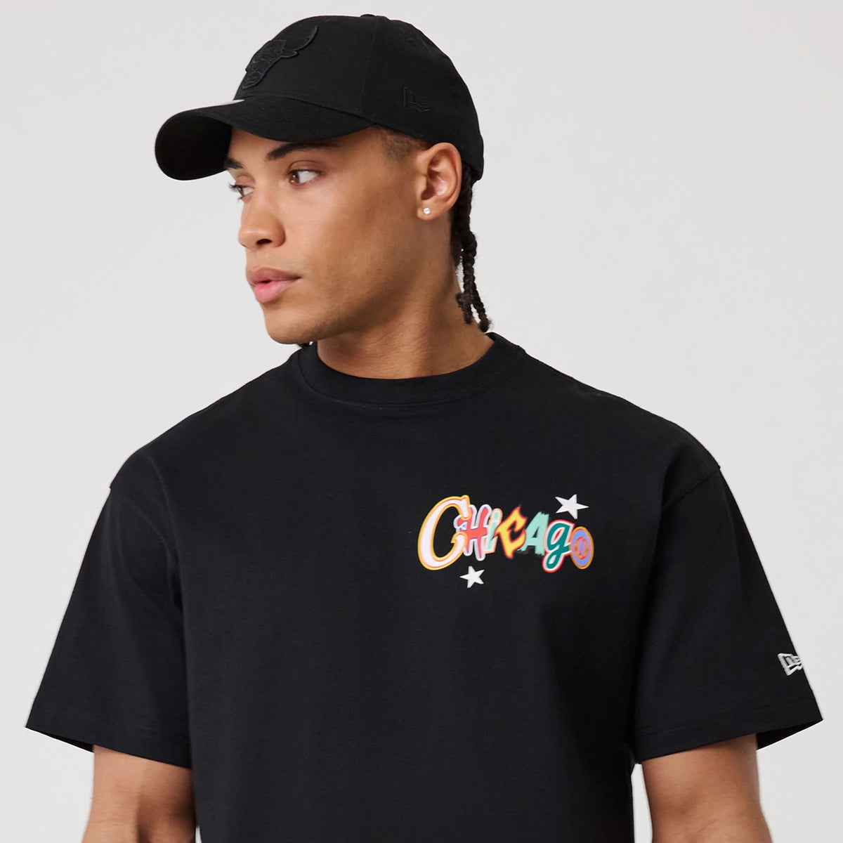 Chicago Bulls MLB Word Art Black T-Shirt, on-model view featuring a colourful "Chicago" word art with stars on the black chest, and a black New Era cap with a debossed logo on the front.