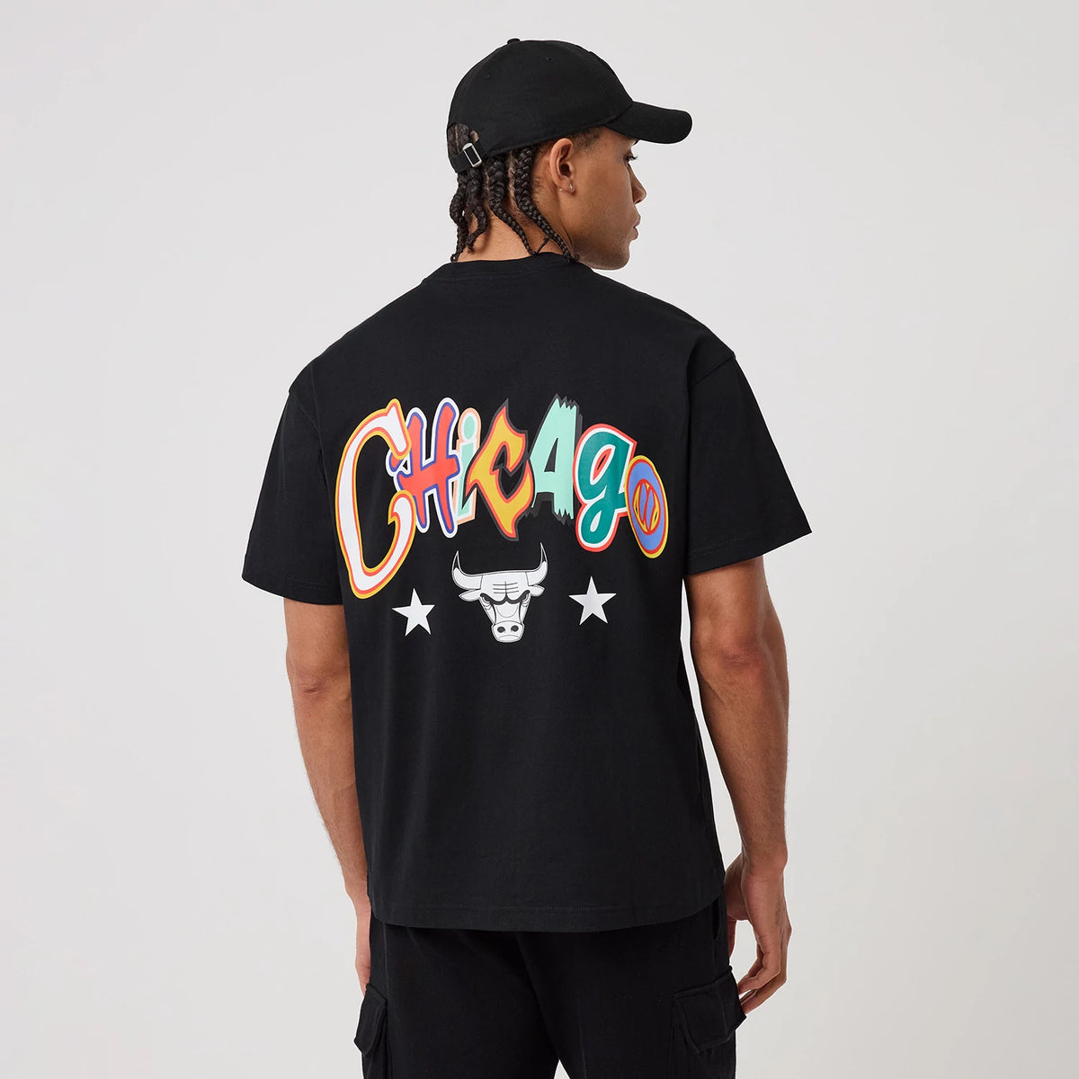 Chicago Bulls MLB Word Art Black T-Shirt, rear view showing a colourful "Chicago" graphic across the upper back, the iconic Bulls logo and two white stars beneath it, worn by a person in black casual attire.