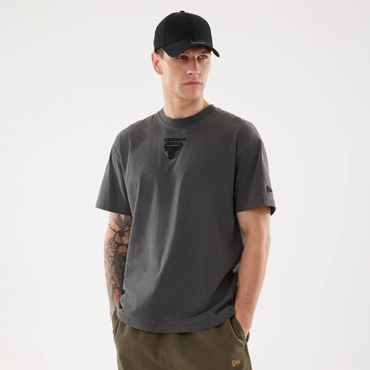 Chicago Bulls NBA Shadow Pop Black T-Shirt, on-model view showing the black debossed Chicago Bulls logo centred on the chest and a small debossed New Era logo on the sleeve, paired with a black cap featuring a raised team logo.