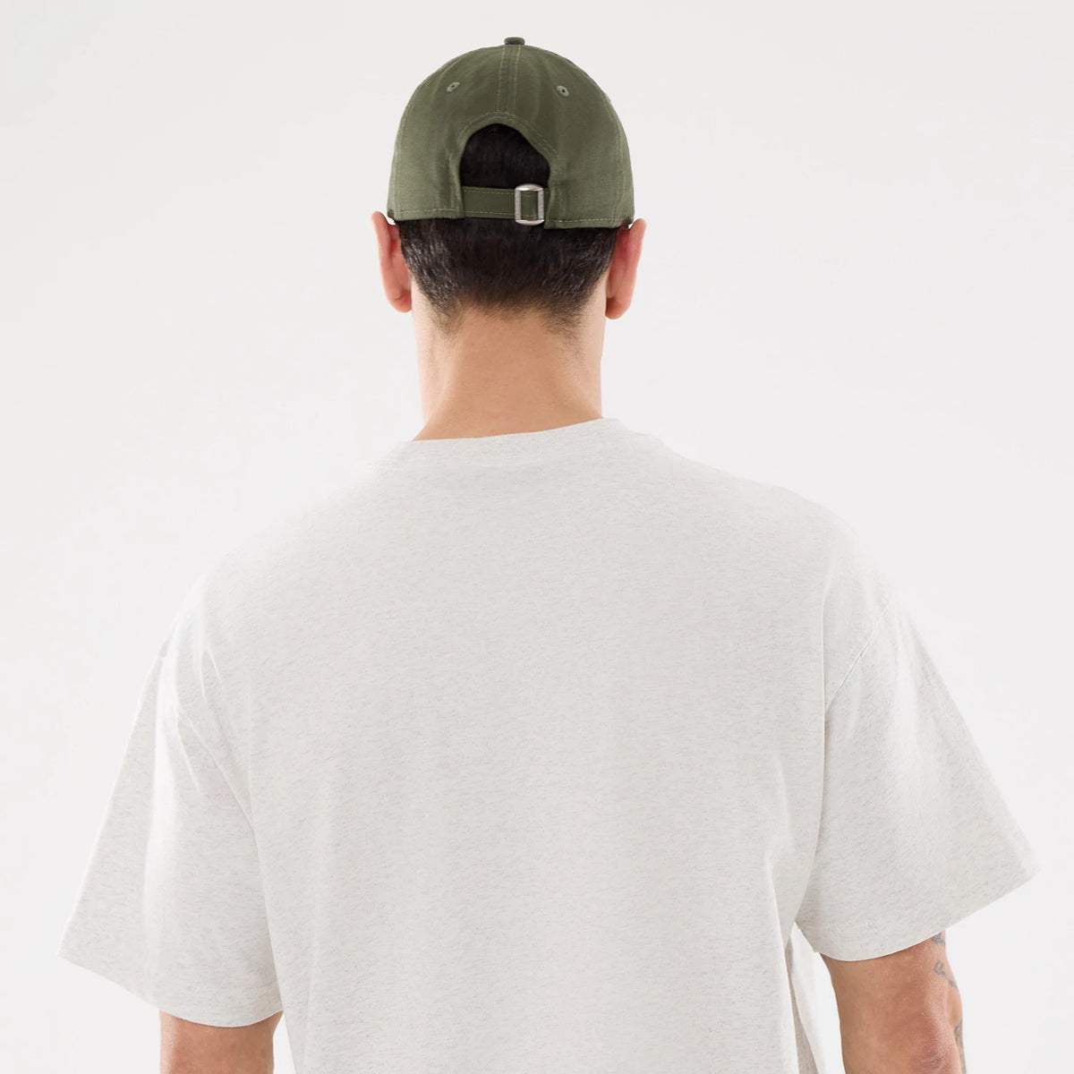 LA Dodgers MLB Comfort Grey T-Shirt, on-model rear view showing the light grey fabric with a plain back, worn with an olive cap featuring a debossed New Era logo, eyelets, and an adjustable strap with a metal buckle.