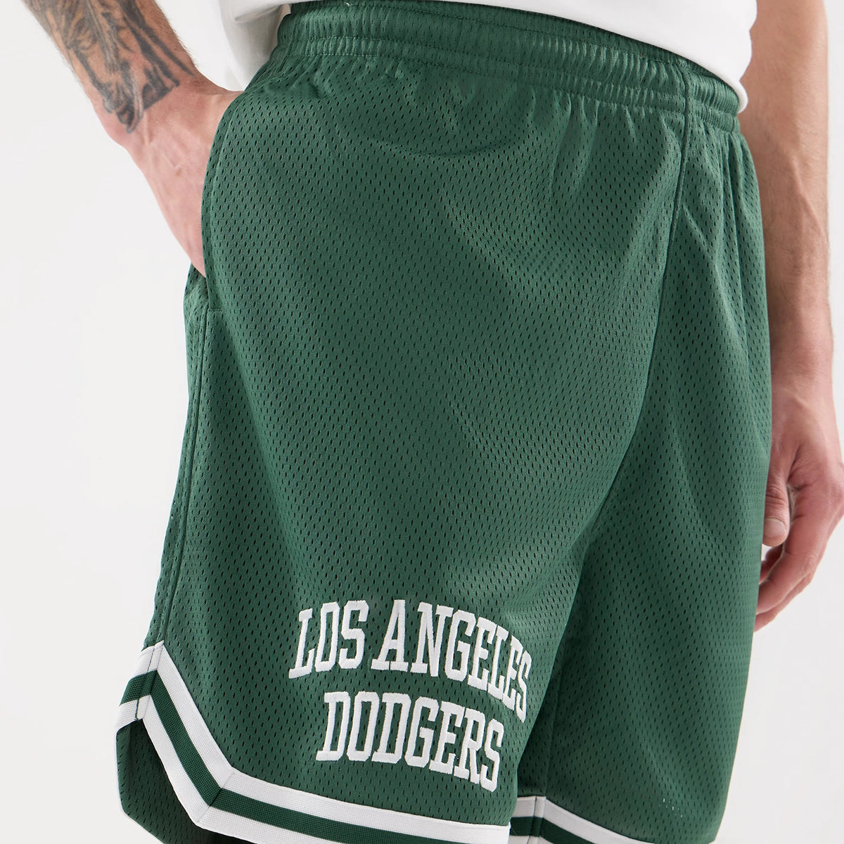 LA Dodgers MLB Comfort Dark Green Oversized Shorts, three-quarter view showing the dark green mesh fabric with a white Los Angeles Dodgers logo embossed on the left leg and a white striped trim at the hem.