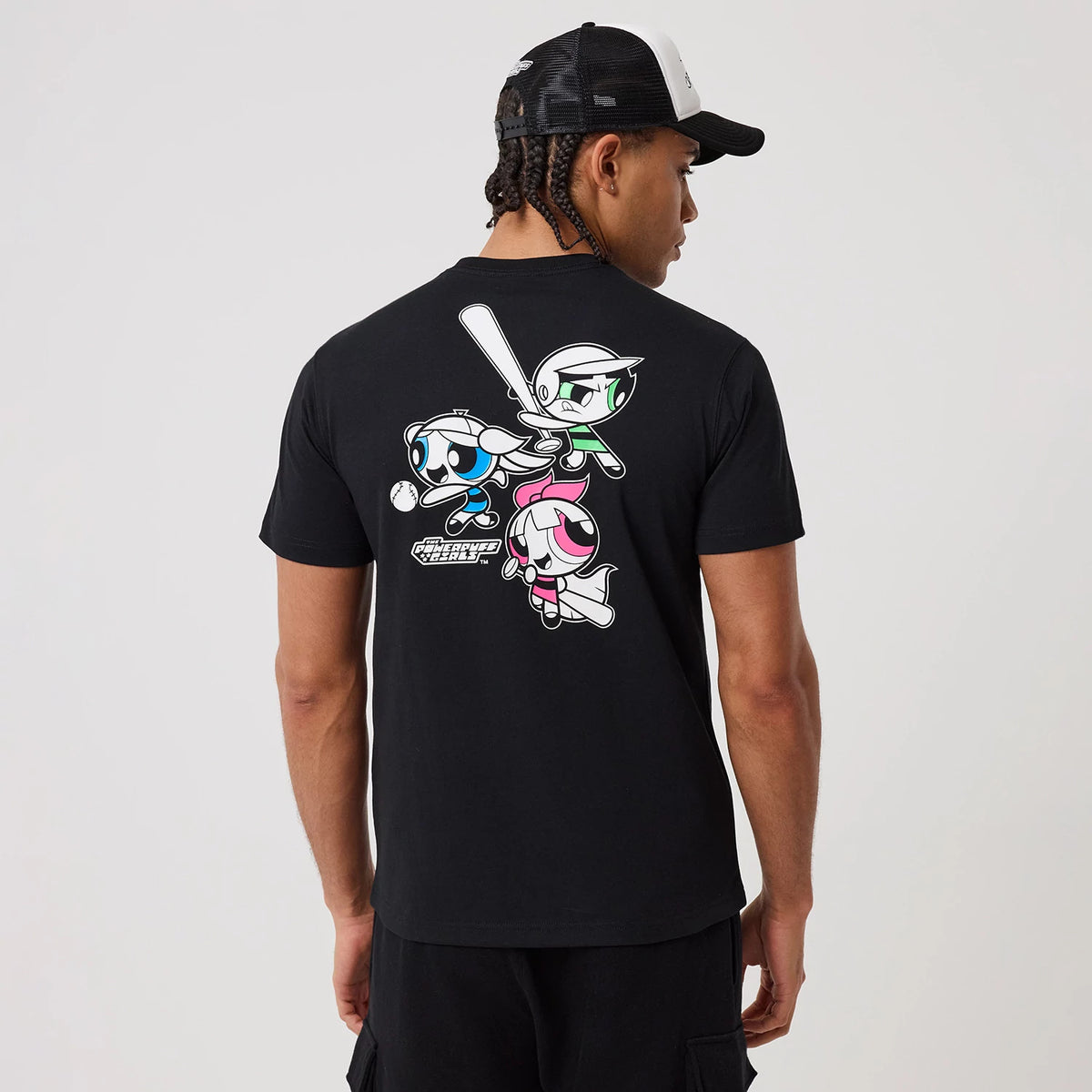 Powerpuff Girls Powerpuff Girls Black T-Shirt, on-model rear view featuring a colourful graphic of the Powerpuff Girls in action poses on the back, worn by a person with a black and white mesh cap.