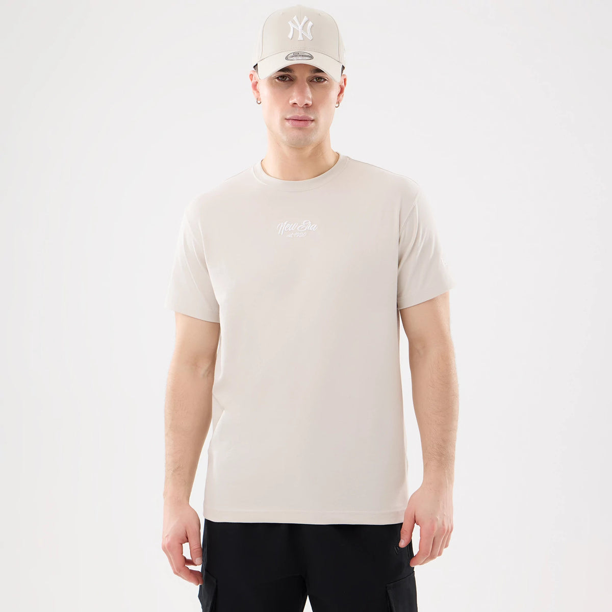 New Era Resort Natural T-Shirt, front view showing the natural-coloured tee with a raised New Era logo centred on the chest, short sleeves, and a man wearing a matching cap with a raised white NY logo on the front.