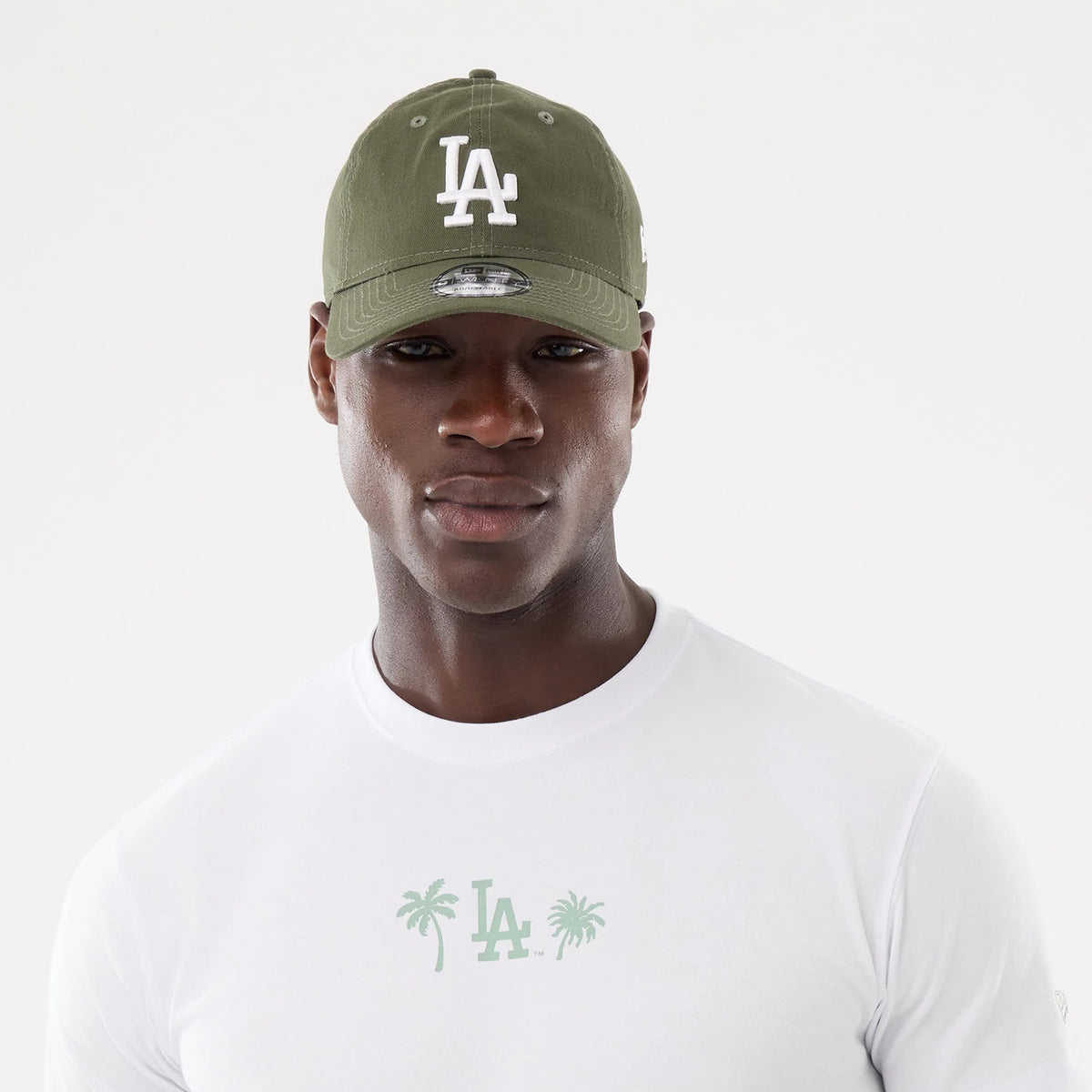 New Era LA Dodgers MLB Resort White T-Shirt, on-model view showing a simple white design with a green LA logo and palm trees on the chest, paired with a green cap featuring a raised white LA logo on the front.