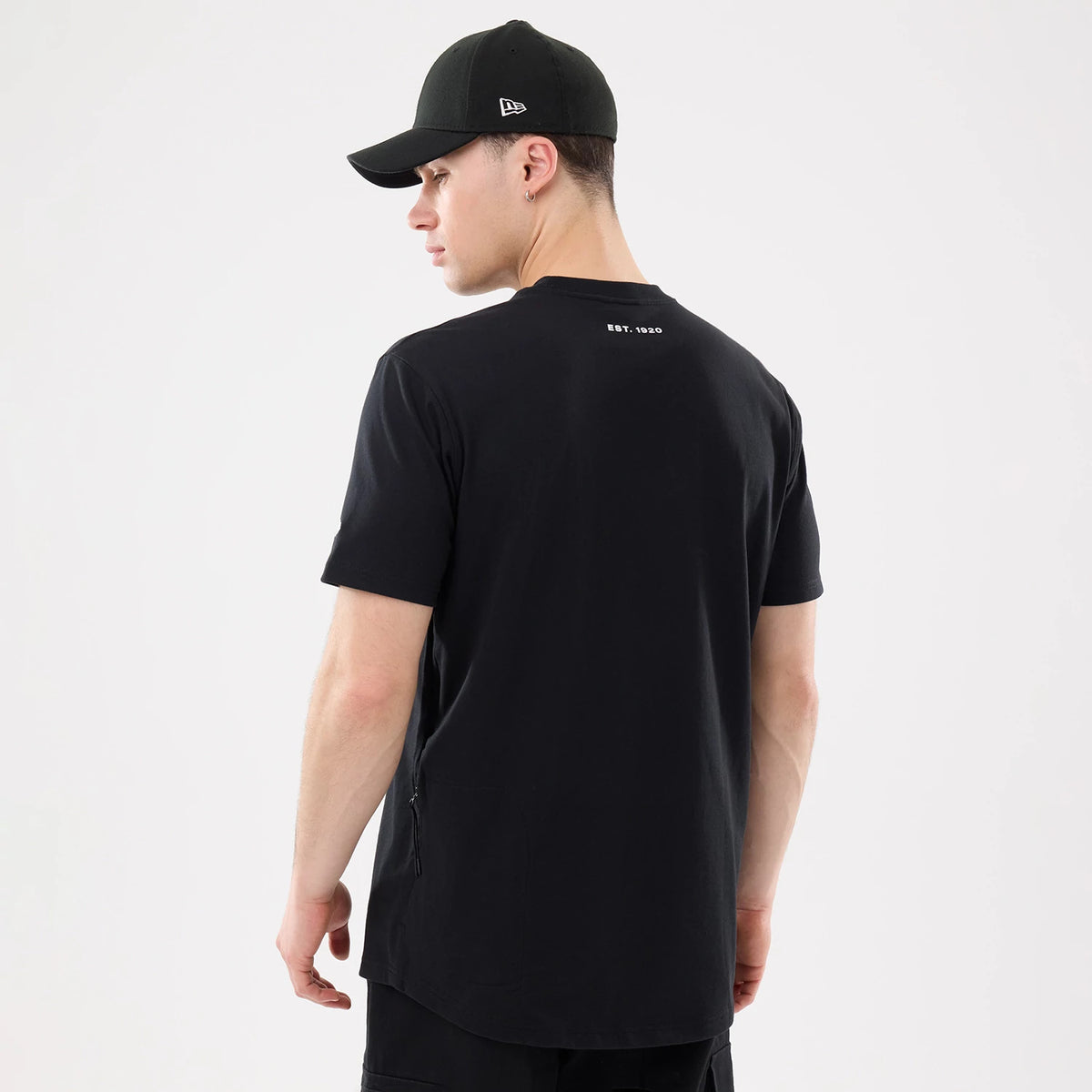 New Era Outdoor Mountain Black T-Shirt, on-model rear view showing the black shirt with white printed text "EST. 1920" below the collar and a black cap with a raised logo on the side worn by the model.