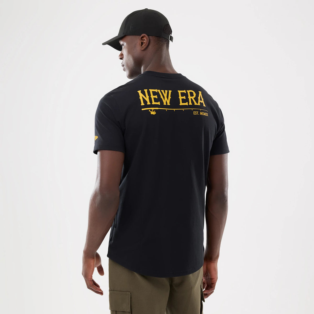 New Era Graphic Outdoor Fishing Black T-Shirt, rear view showing a large yellow "New Era" graphic across the upper back, a small logo on the sleeve, and a man wearing a black cap paired with the t-shirt.