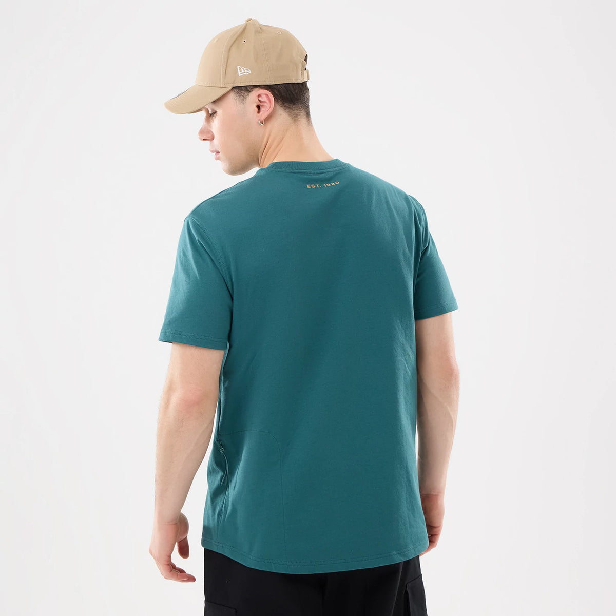 New Era Outdoor Mountain Dark Green T-Shirt, on-model rear view showing a man wearing the dark green T-shirt with "Est. 1920" embossed on the upper back, paired with a beige cap featuring a raised New Era logo on the side.