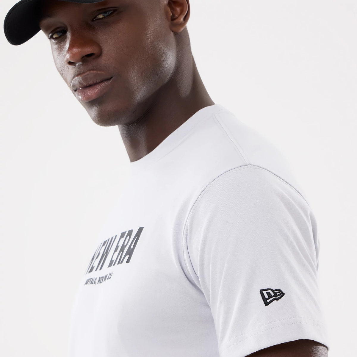 New Era Basic White T-Shirt, on-model view showing a close-up of the white shirt with a large printed black New Era logo across the chest, a small embroidered black New Era logo on the left sleeve and short sleeves.