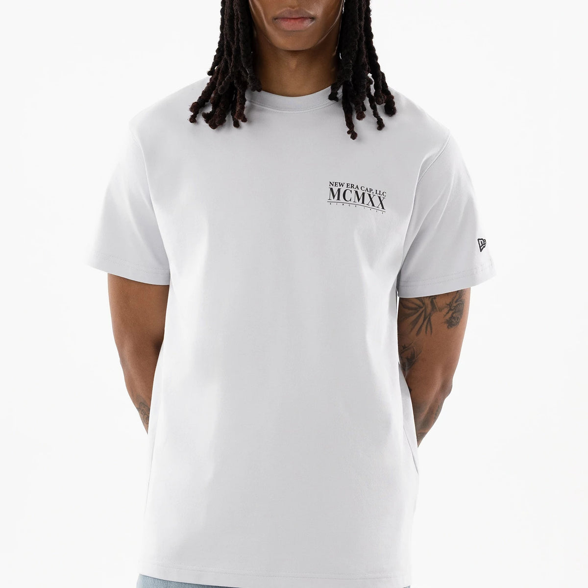 New Era Heritage White T-Shirt, front view showing the white shirt with a black printed logo on the left chest reading 'New Era Cap L.L.C. MCMXX,' featuring short sleeves and a small embroidered New Era logo on the left sleeve.