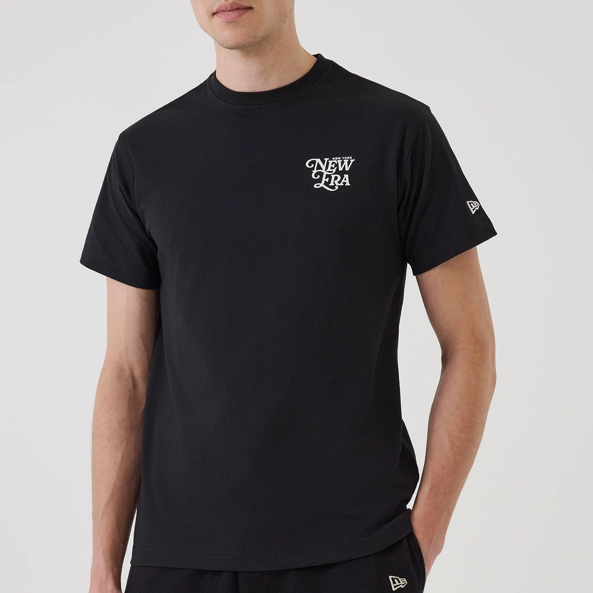New Era Script Graphic Black T-Shirt, on-model view showing the black short-sleeve tee with a raised white New Era logo on the left chest and a small raised New Era flag logo on the left sleeve.