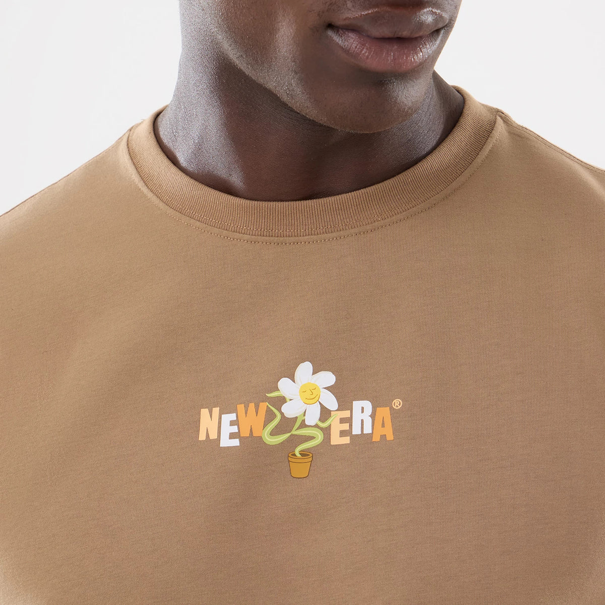 New Era Earth Day Beige T-Shirt, front view featuring a centred daisy graphic with a smiling face in a pot, the words "NEW ERA" in block letters integrated into the design on a beige fabric backdrop.