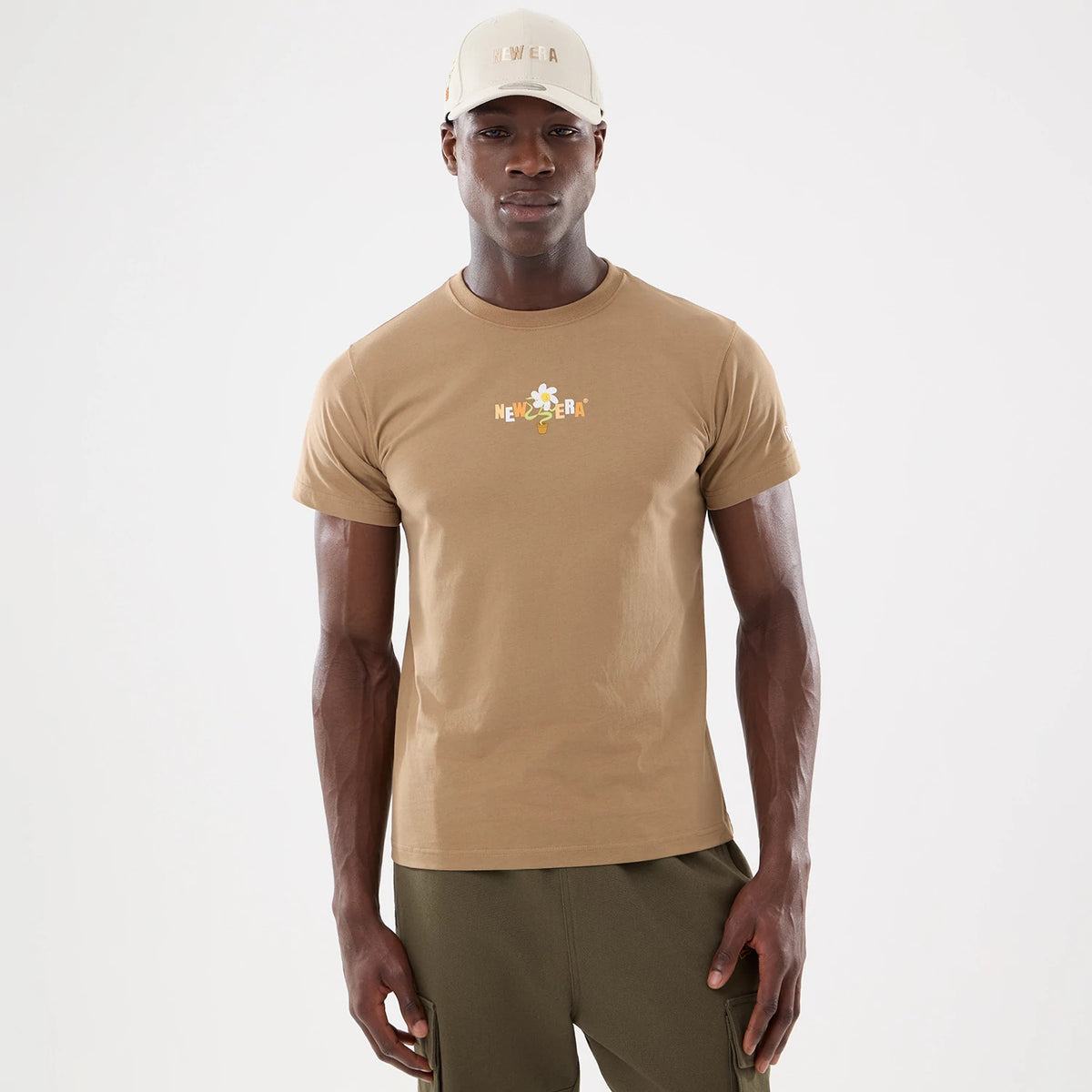 New Era Earth Day Beige T-Shirt, on-model view showing the beige T-shirt with a colourful flower and New Era logo centred on the chest, paired with a beige cap featuring a raised logo on the front.