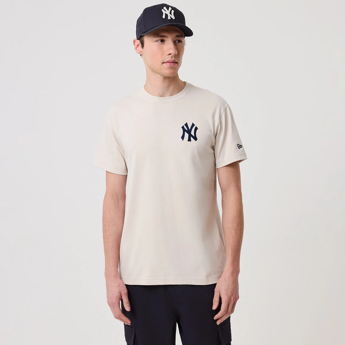New York Yankees MLB Banana Graphic Natural T-Shirt, on-model view showing a cream coloured T-shirt with a dark blue embroidered Yankees logo on the left chest and a New Era logo on the left sleeve, worn with a matching cap featuring the same logo.