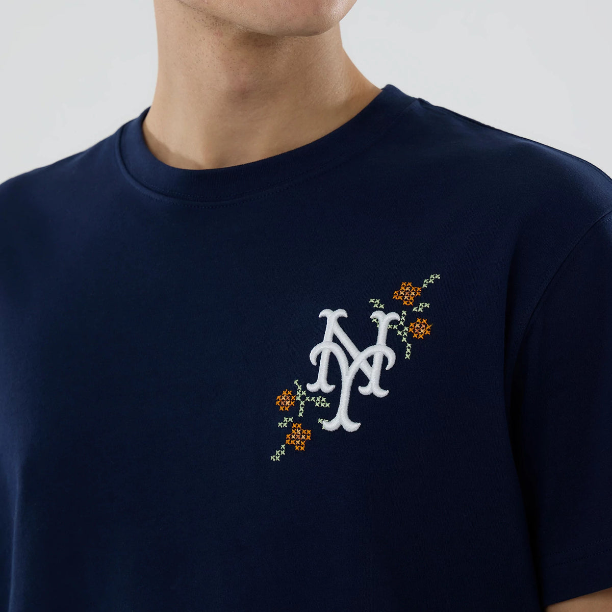 New York Mets MLB Garden Blue T-Shirt, front view showing the embroidered white New York Mets logo on the chest with decorative floral accents in orange and green on a navy blue background.