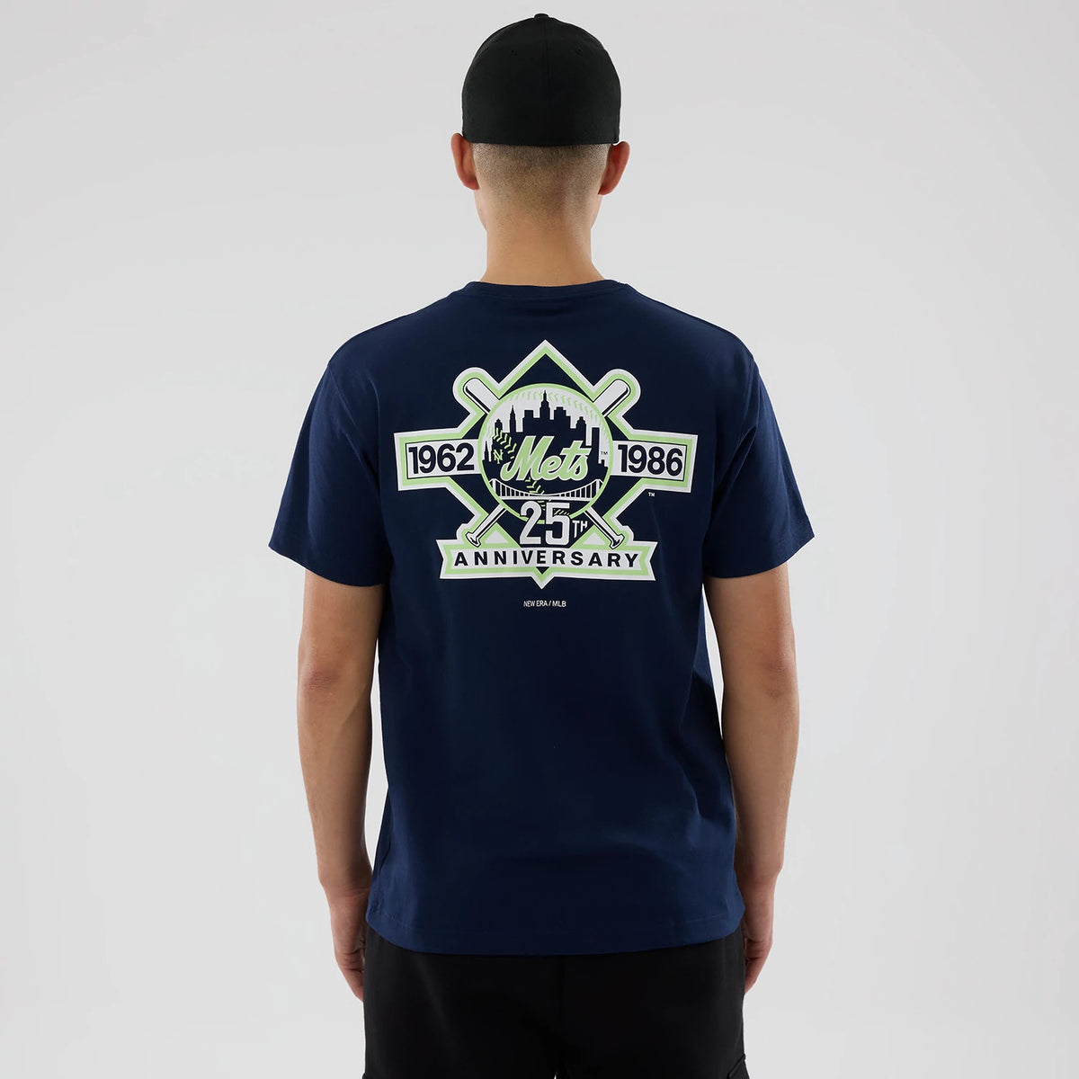 New York Mets MLB Garden Blue T-Shirt, rear view showing a large graphic design featuring crossed bats, "Mets" script, "1962," "1986," "25th Anniversary" lettering, and a skyline with green accents on the dark blue fabric.