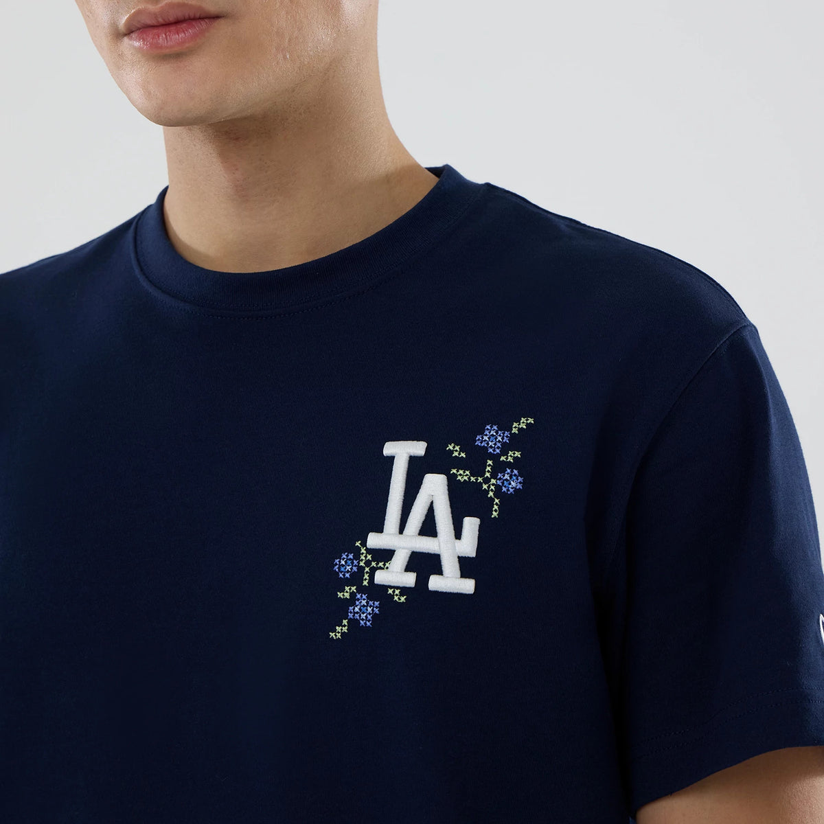 LA Dodgers MLB Garden Blue T-Shirt, on-model view showing the white embossed LA Dodgers logo on the left chest with floral embroidery in blue and green extending from the logo on a dark blue fabric.