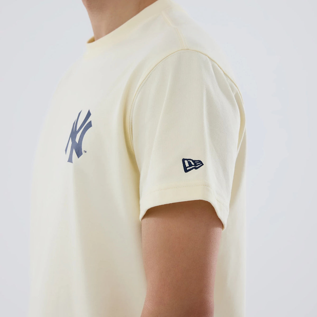 New York Yankees MLB City Series Cream T-Shirt, side view showing the short sleeve with a raised New Era logo on the arm and a large raised New York Yankees logo on the chest of the cream fabric.