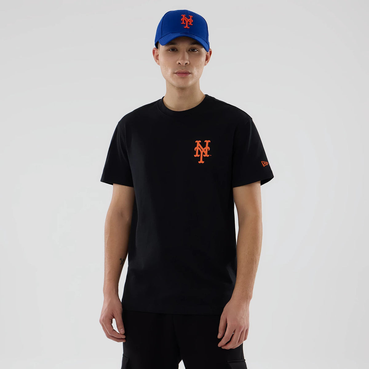 New York Mets MLB City Series Black T-Shirt, on-model view showing a black T-shirt with an orange embossed Mets logo on the chest, paired with a blue cap featuring the same logo, and a raised New Era logo on the sleeve.
