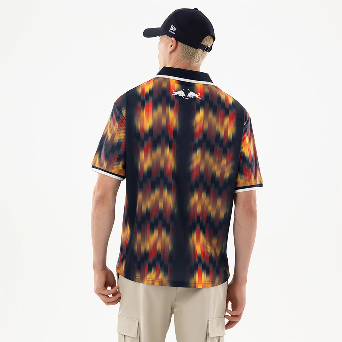 New Era Red Bull Racing Multi Soccer Jersey, back view on a model wearing a black cap, featuring a dynamic multicoloured pattern with a prominent Red Bull logo across the upper back and contrasting black collar and sleeve trims.