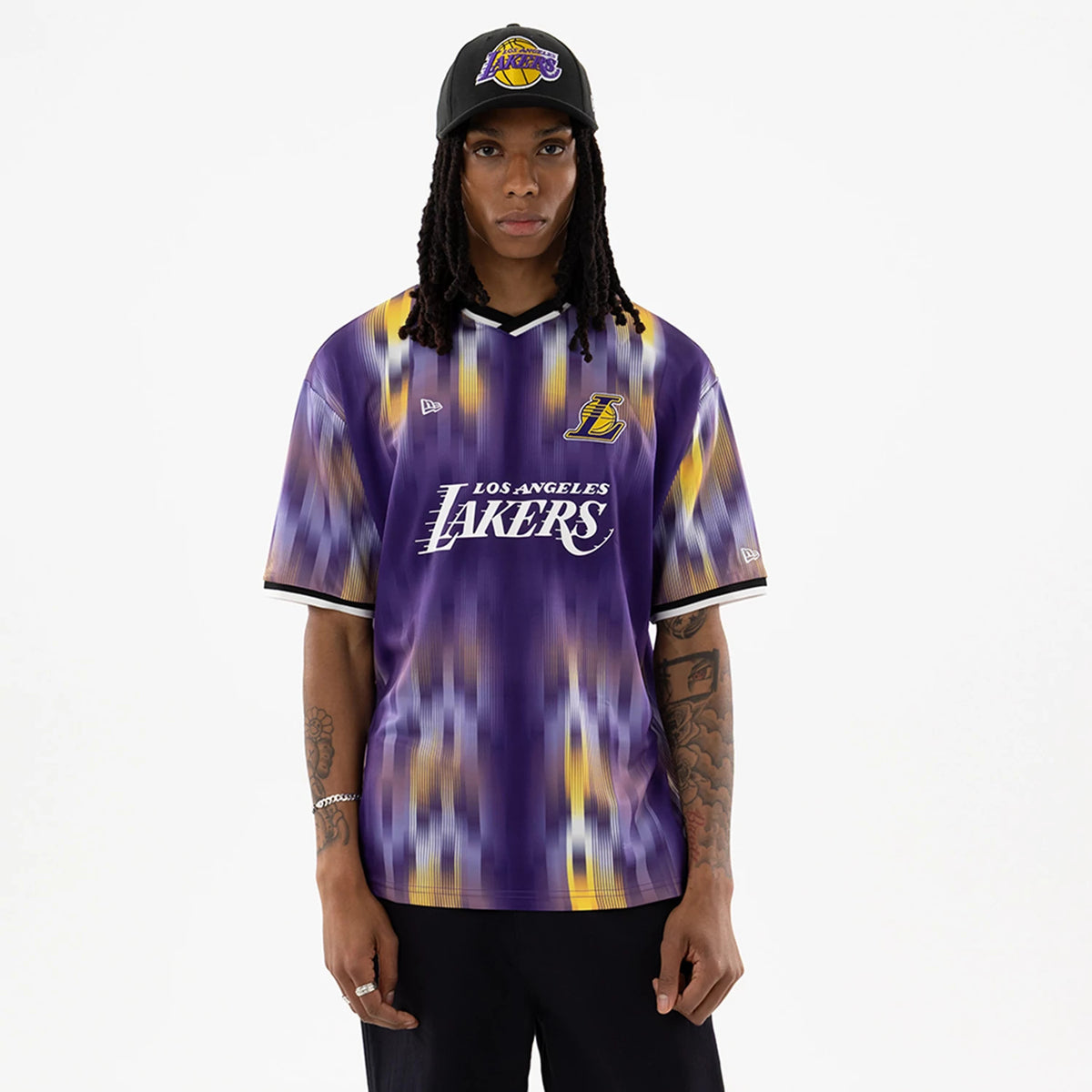 LA Lakers NBA Purple Soccer Jersey, front view on a model wearing a black cap, featuring the yellow L logo and white Los Angeles Lakers lettering on the chest, with a blurred pattern and black-trimmed sleeves.