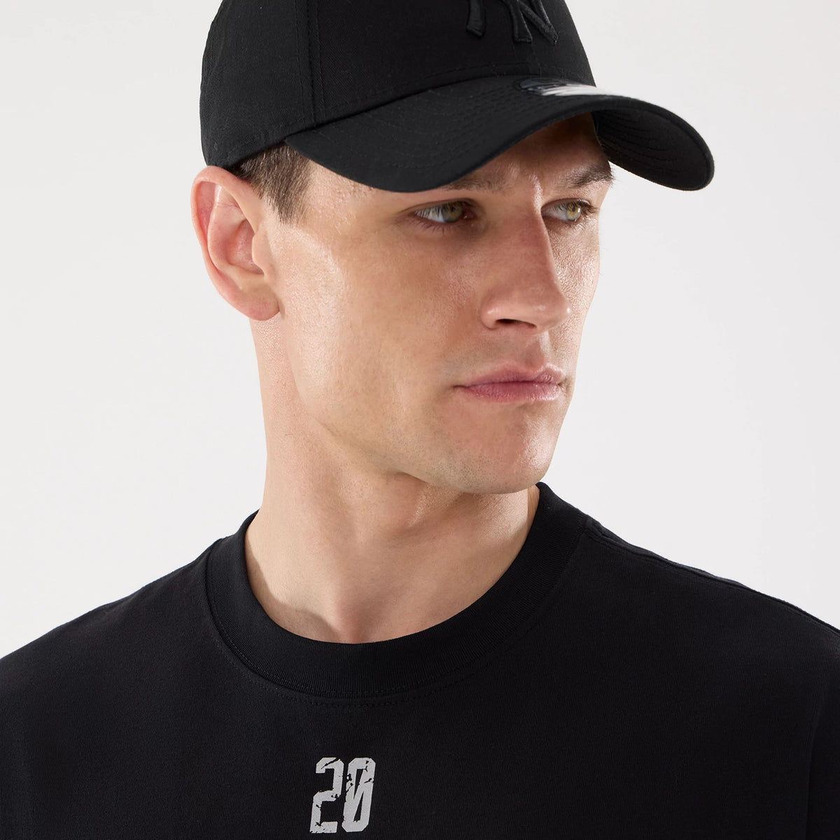 New Era Graphic Street Archived City Black Oversized T-Shirt, on-model view showing a black shirt with a white numeric graphic on the chest, paired with a black cap featuring a raised logo on the front.