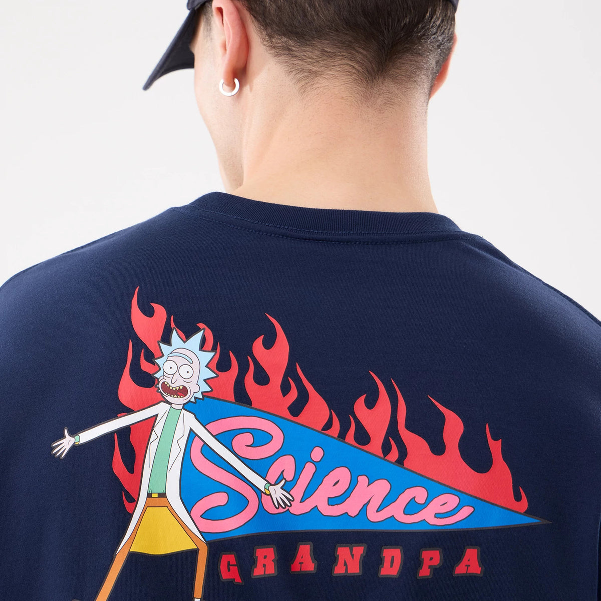 New Era Rick And Morty Blue T-Shirt, rear view featuring a colourful graphic of a character with spiky blue hair next to red and blue text saying Science Grandpa amidst red flame designs on the dark blue fabric.