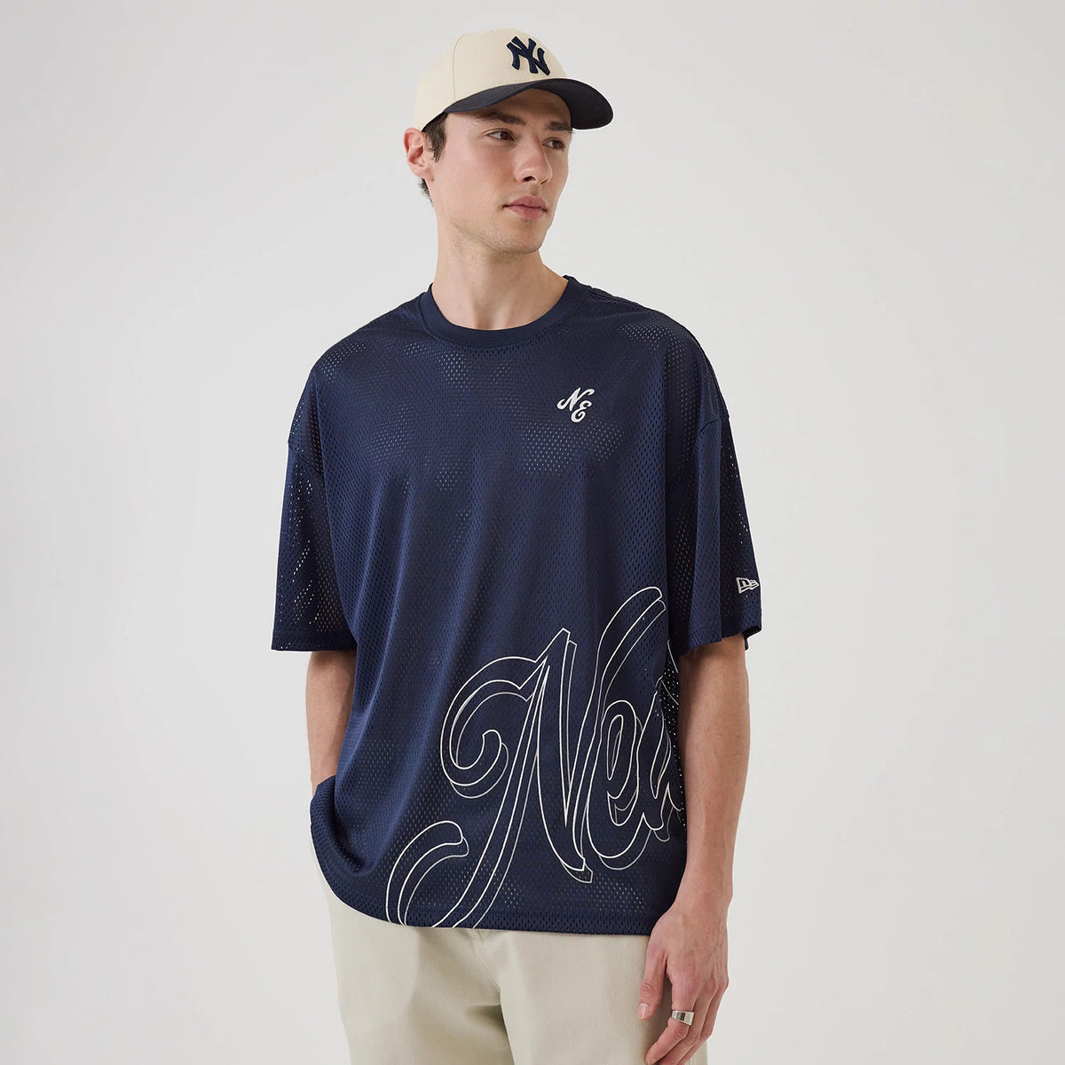 New Era Mix League Blue Oversized Mesh T-Shirt, on-model view showing a navy mesh design with a large script logo across the lower front, a small embroidered logo on the chest, and a debossed New Era logo on the left sleeve.