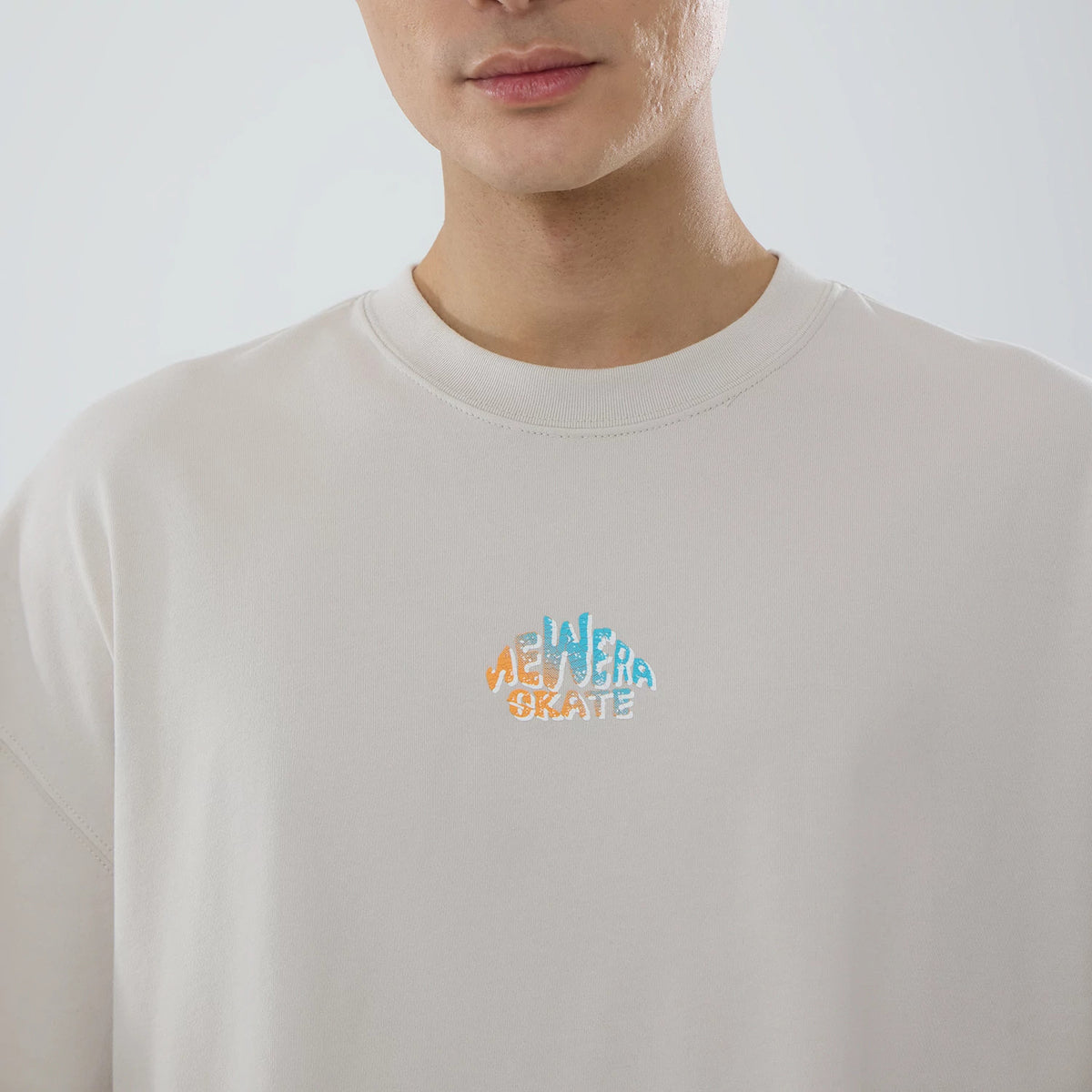 New Era Skate Is Life Graphic Cream Oversized T-Shirt, front view showing the cream fabric with a central multicoloured raised logo displaying "New Era Skate" in blue, orange, and white on the chest just below the neckline.