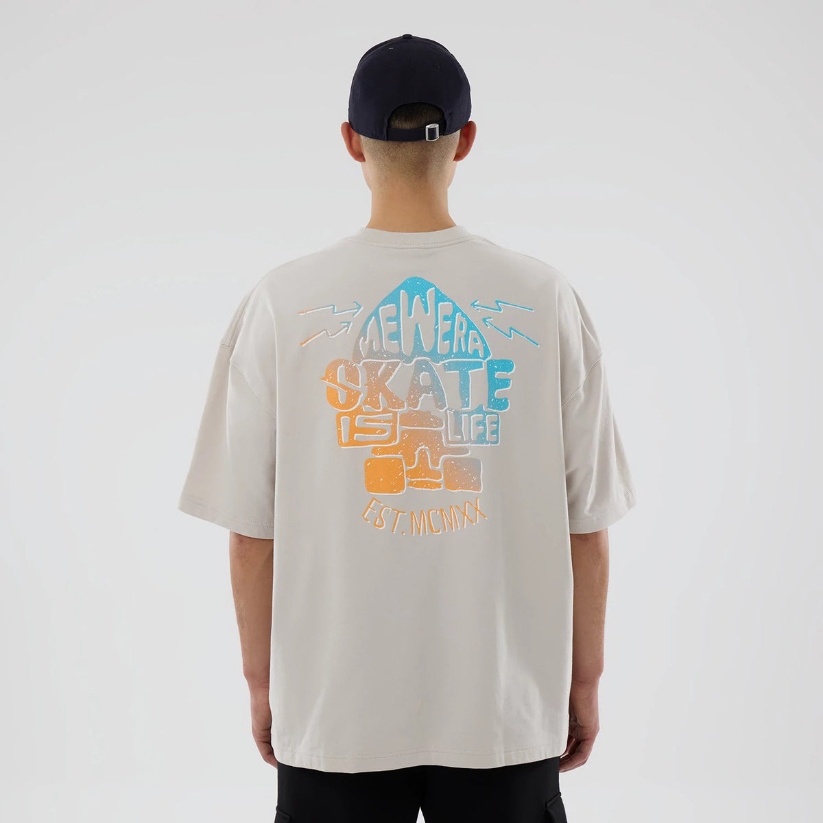 New Era Skate Is Life Graphic Cream Oversized T-Shirt, rear view showing the colourful graphic design centred on the back with "Skate Is Life" and "Est. MCMXX" text in various pastel shades over the cream fabric.