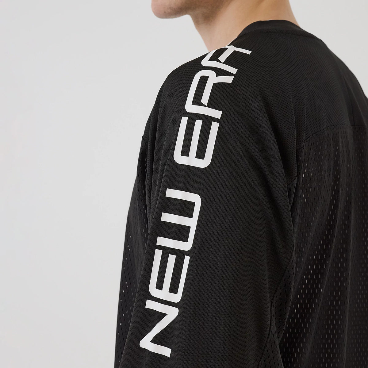New Era NEC Logo Black Long Sleeve Jersey, side view on a model showing the white New Era lettering vertically along the right sleeve, with perforated detailing on the black fabric and the shoulder seam visible.