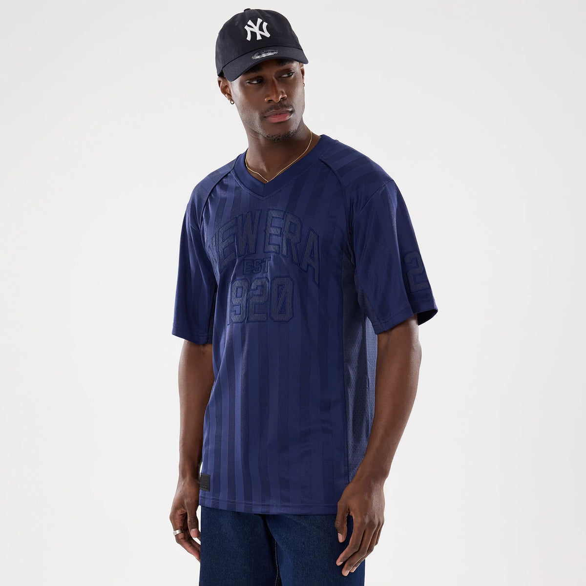 New Era Street Archived Navy Mesh Jersey, on-model showing a navy blue v-neck design with tonal vertical stripes and New Era EST 1920 lettering across the chest, paired with a dark cap featuring an embroidered white NY logo.