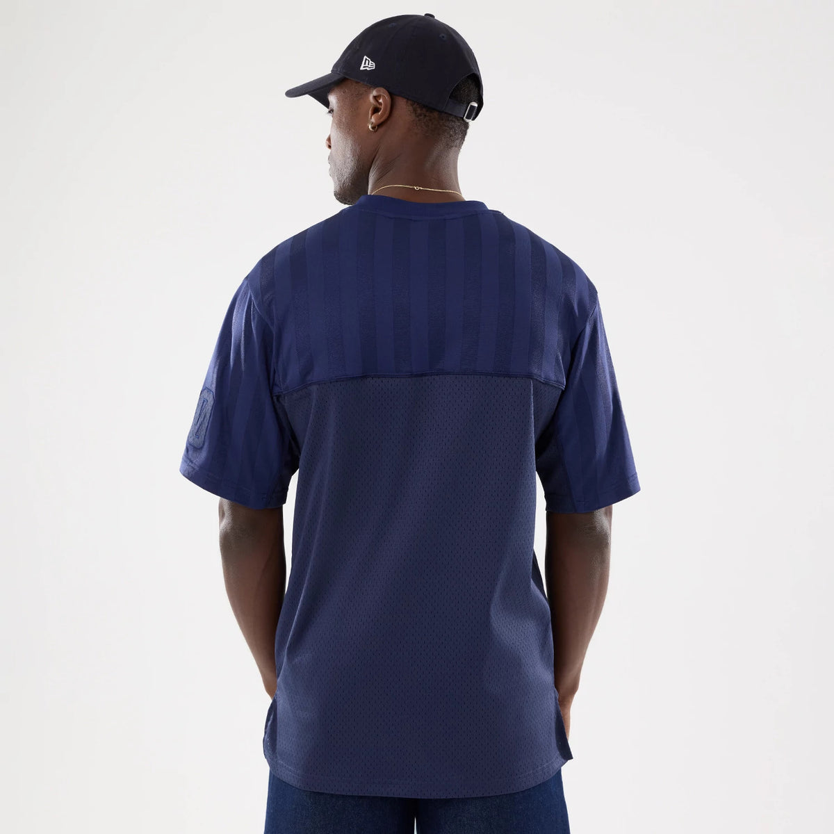 New Era Street Archived Navy Mesh Jersey, back view on a model wearing a matching navy cap, featuring tonal stripe detailing across the shoulders and a textured mesh fabric on the lower back panel.