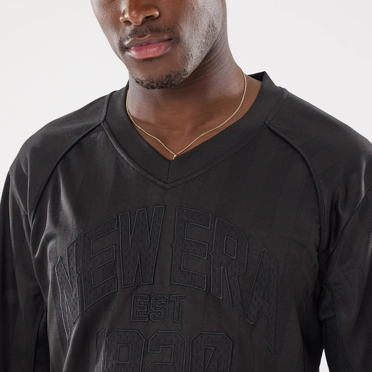 New Era Street Archived Black Mesh Jersey, front view on a model wearing a gold chain, featuring raised black New Era EST 1920 lettering on the chest below the V-neckline and textured fabric details.