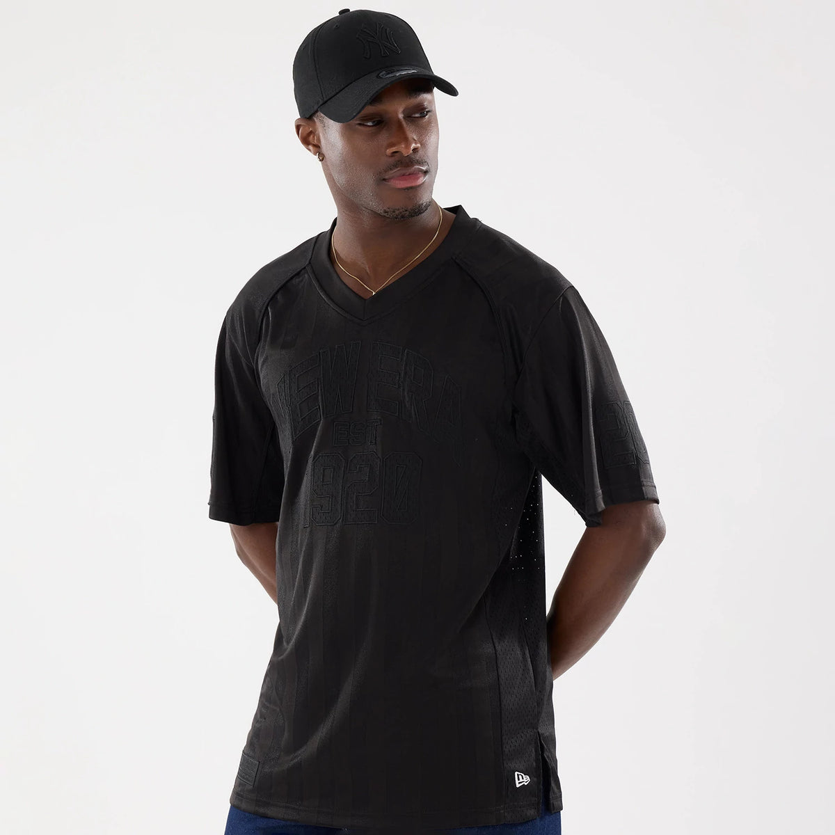 New Era Street Archived Black Mesh Jersey, front view on a model wearing a black cap, featuring raised New Era EST 1920 lettering across the chest, a V-neck design, and the New Era flag logo on the bottom hem.