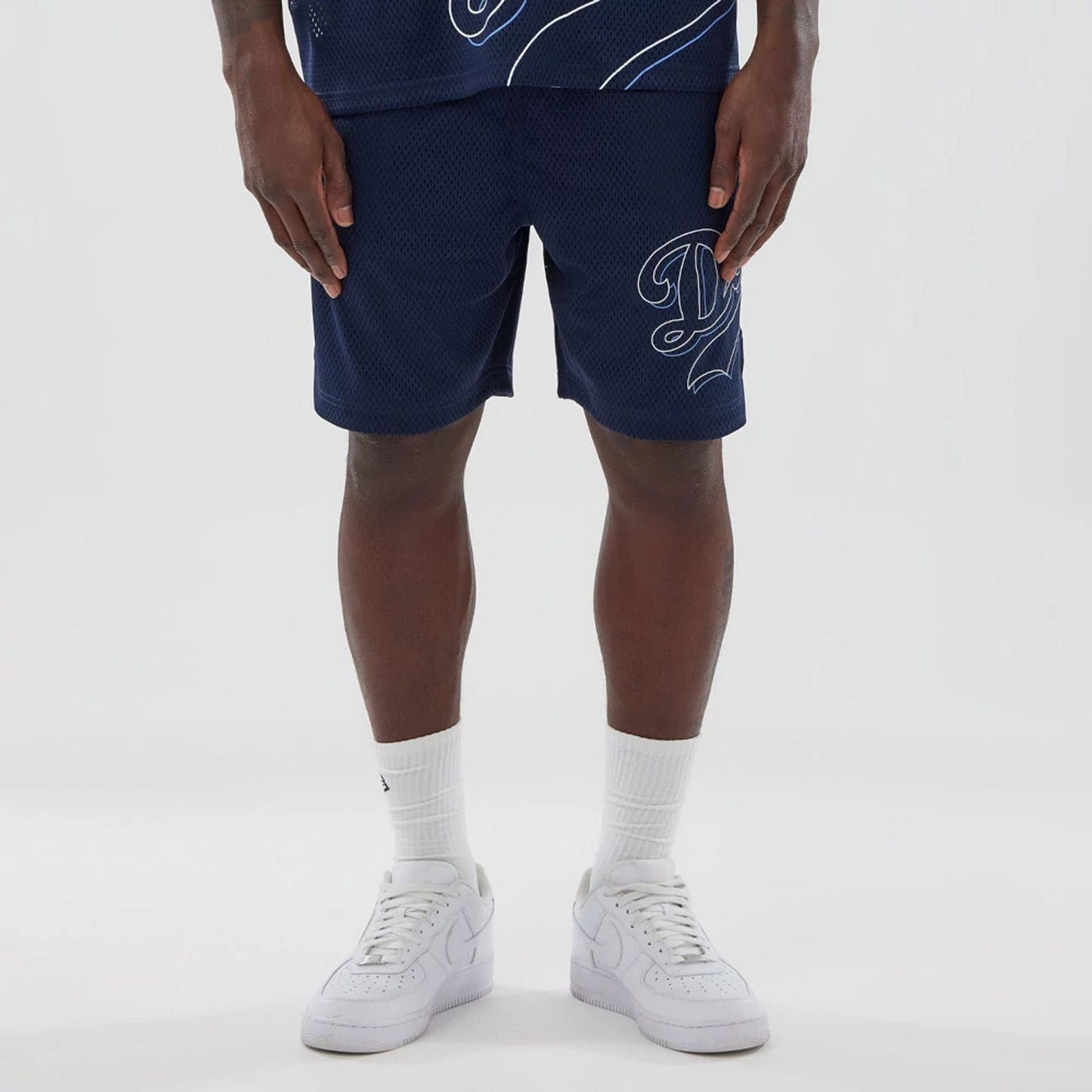 LA Dodgers MLB Mix League Blue Oversized Mesh Shorts, front view showing the navy mesh fabric with a large white script "D" logo on the left leg, worn mid-thigh length with white socks and sneakers.