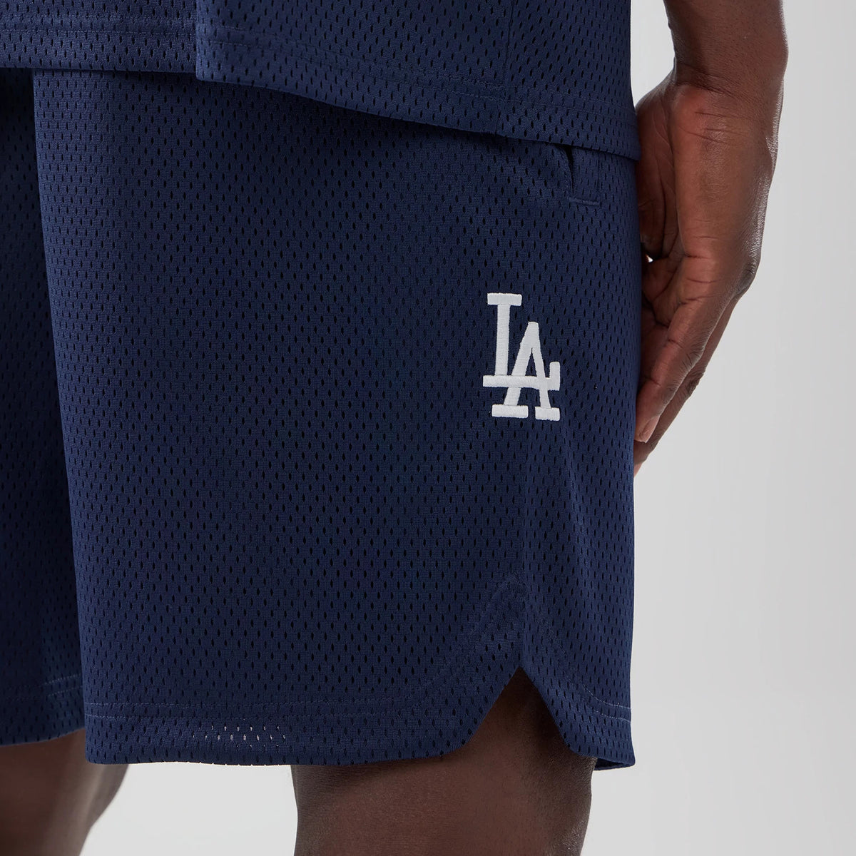 LA Dodgers MLB Mix League Blue Oversized Mesh Shorts, side view showing the navy mesh fabric with a white raised LA logo on the lower leg near the hem, worn by a model with the hand resting by the side.