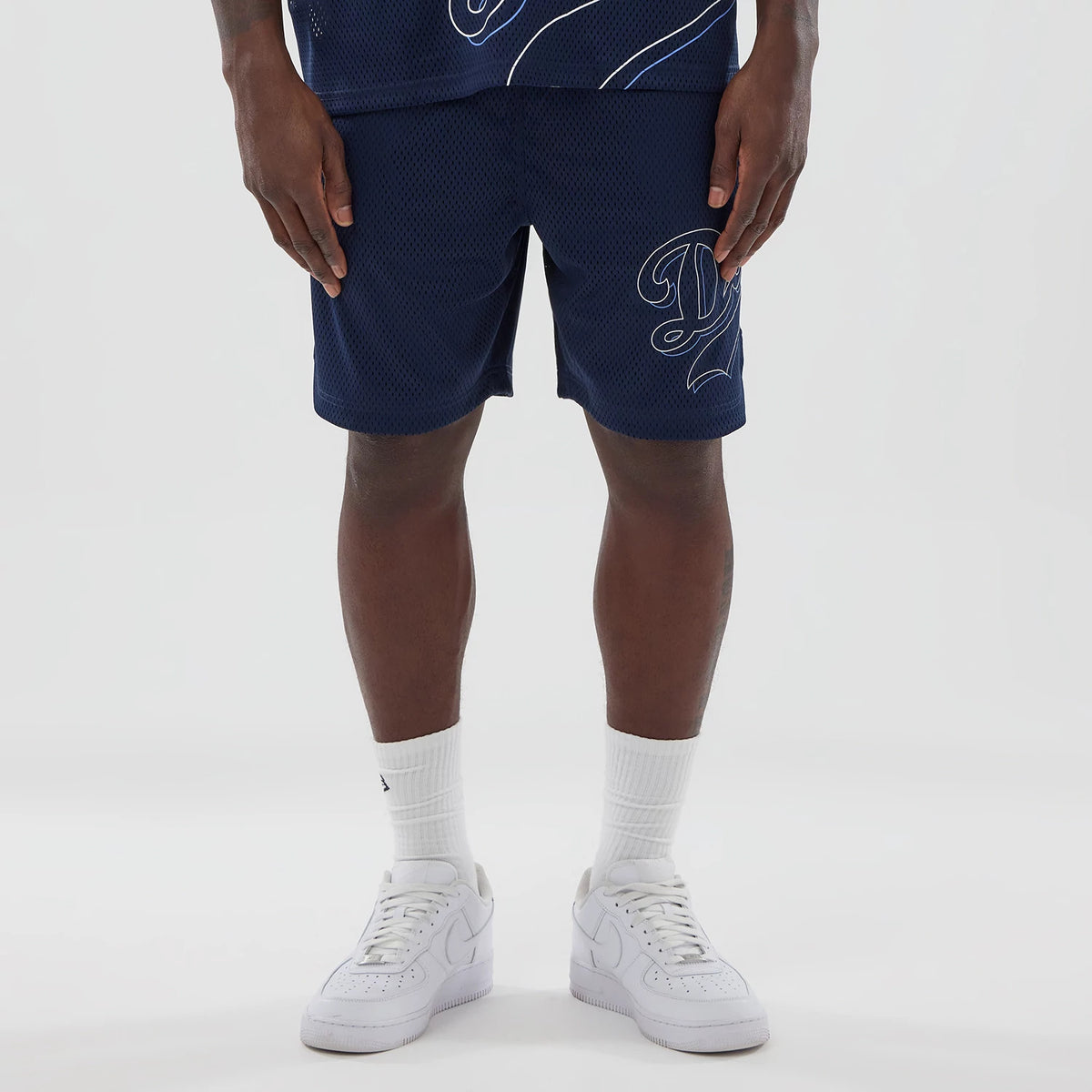 LA Dodgers MLB Mix League Blue Oversized Mesh Shorts, front view showing dark blue mesh fabric with a large white embroidered "D" logo on the right thigh, worn by a model with white sneakers and socks.