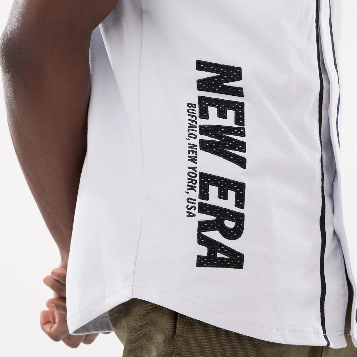 New Era Basic White Jersey, side view on a model showing black embroidered New Era lettering down the right side with Buffalo, New York, USA text beneath, paired with olive green trousers.