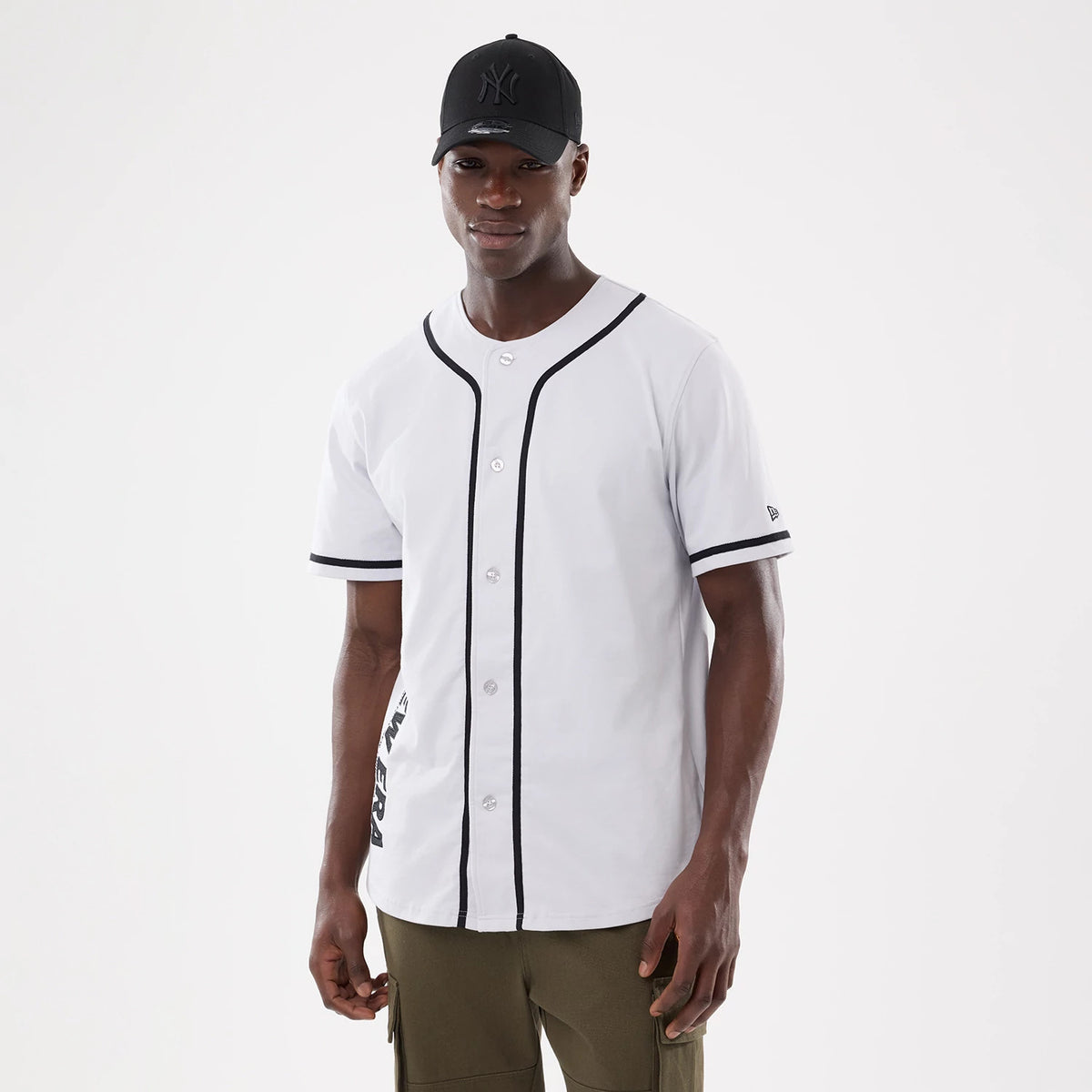 New Era Basic White Jersey, front view on a model wearing a black cap, featuring black piping along the buttoned placket, short sleeves with black trim, and New Era branding on the left sleeve.