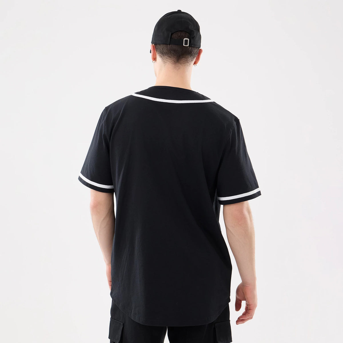 New Era Basic Black Jersey, back view on a model wearing a matching black cap with a structured crown and adjustable strap, showing white trim on the sleeves and collar for a classic look.