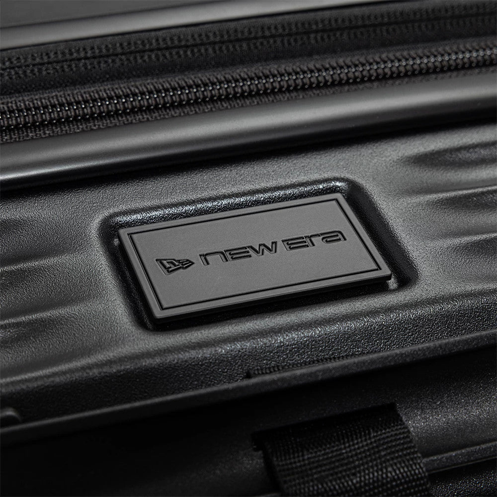 New Era Black Wheeled Cabin Case, close-up view showing a rectangular debossed New Era logo centred on the textured black surface, with a zip closure detail running horizontally above the logo.