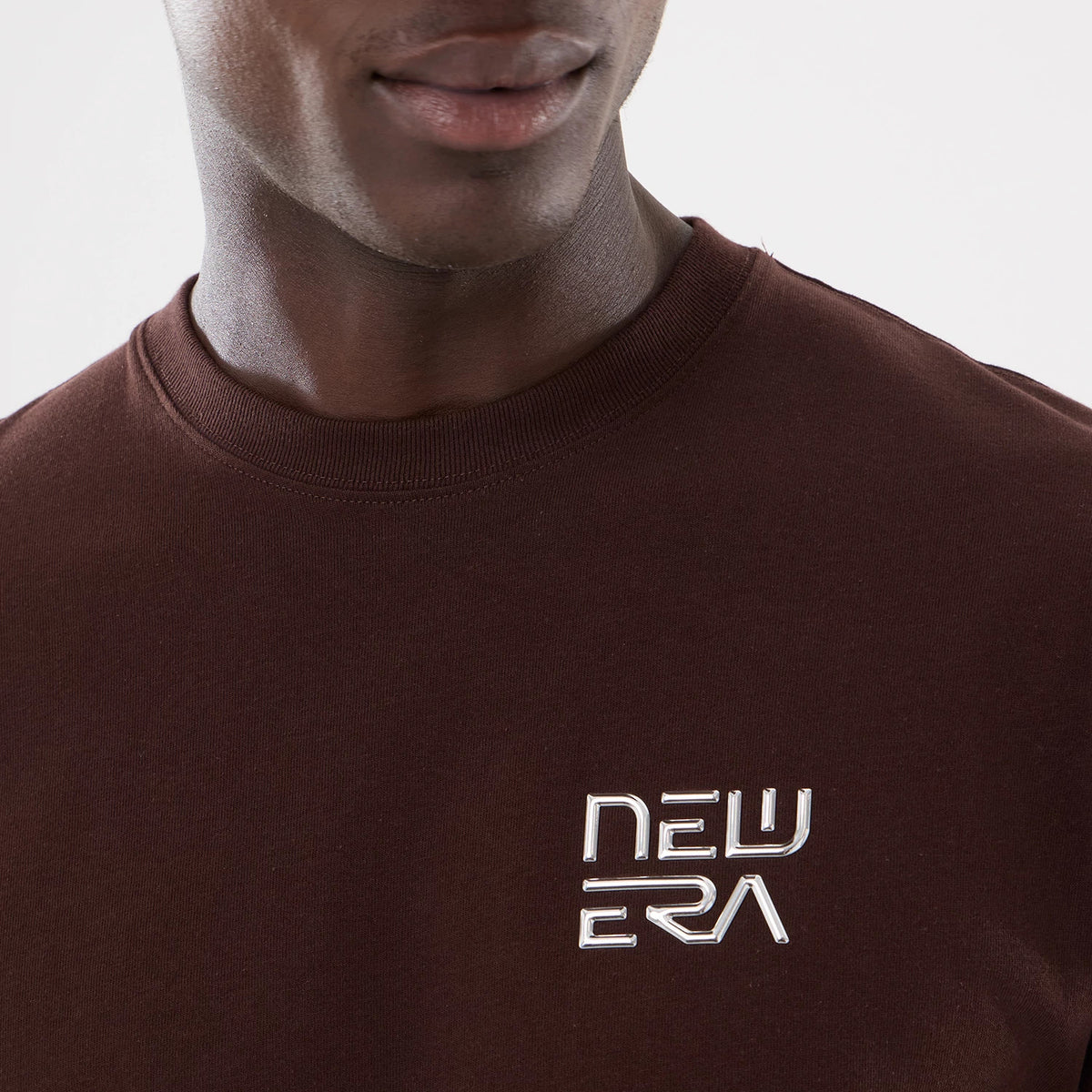 San Diego Padres Hajime Sorayama X MLB Dark Brown T-Shirt, on-model view showing the chest area with a raised New Era logo in silver positioned on the left side against the plain dark brown fabric.