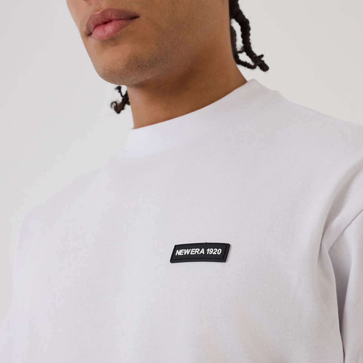 New Era Distressed White T-Shirt, on-model view showing the simple white design with a raised New Era 1920 logo patch on the left chest, captured from the shoulder to the upper chest area.