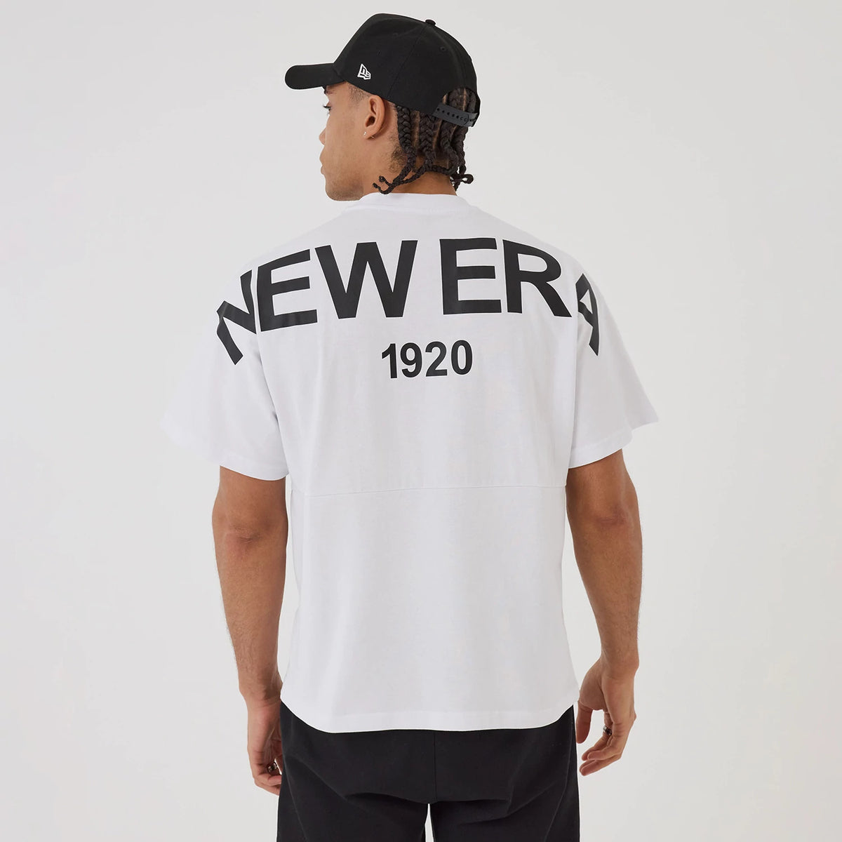 New Era Distressed White T-Shirt, on-model view showing the back of the oversized white shirt with bold black "NEW ERA" text and "1920" printed below, worn by a person in a black cap.